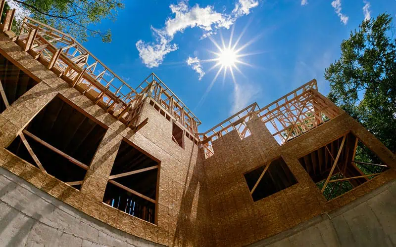 Innovative house under construction with wooden framing and modern design, set against a bright blue sky with the sun shining, showcasing contemporary architecture by RMO Agency.