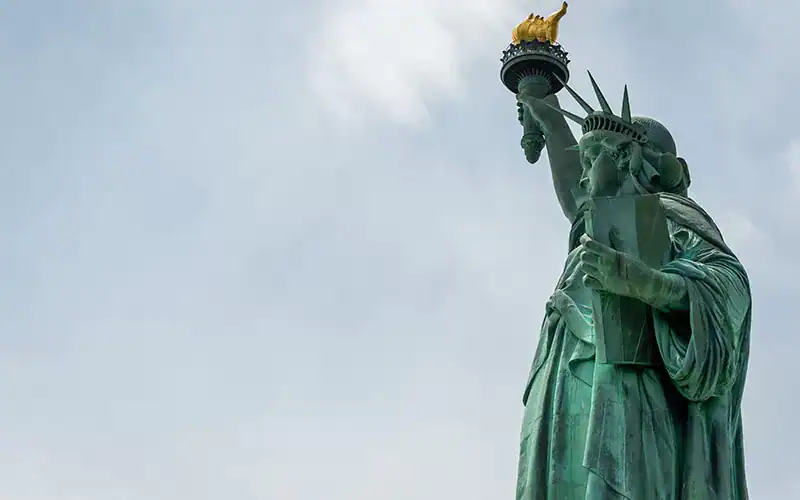 Historic Statue of Liberty with cloudy sky background.
