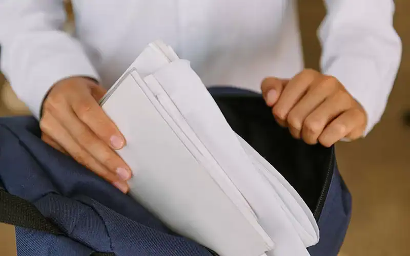 Professional business person packing documents into a navy backpack for meetings or travel.