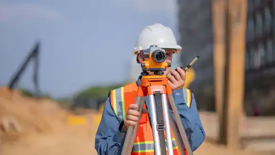 Surveyor using a theodolite at construction site.