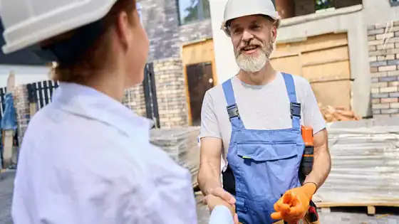 Experienced construction worker shaking hands with a colleague at a building site for roofing and construction services.