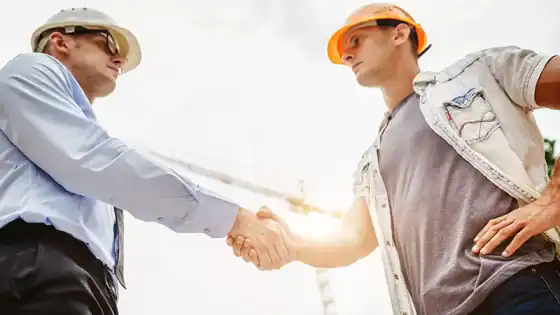 Construction professionals shaking hands at a building site, symbolizing partnership and collaboration in the construction industry.