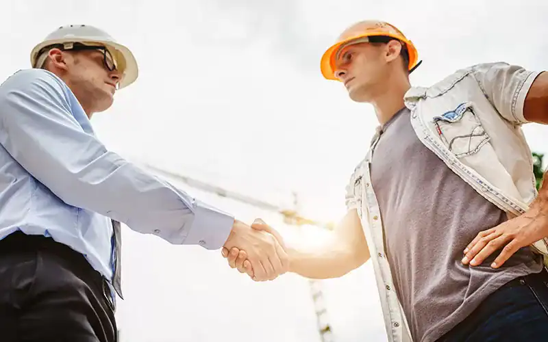 Construction professionals shaking hands at a building site, symbolizing partnership and collaboration in the construction industry.