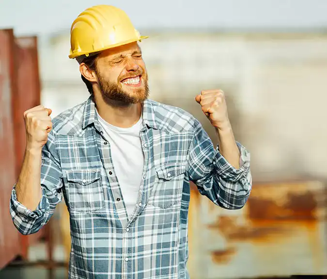 Hardhat-wearing construction worker celebrating success at building site, expressing achievement and confidence.
