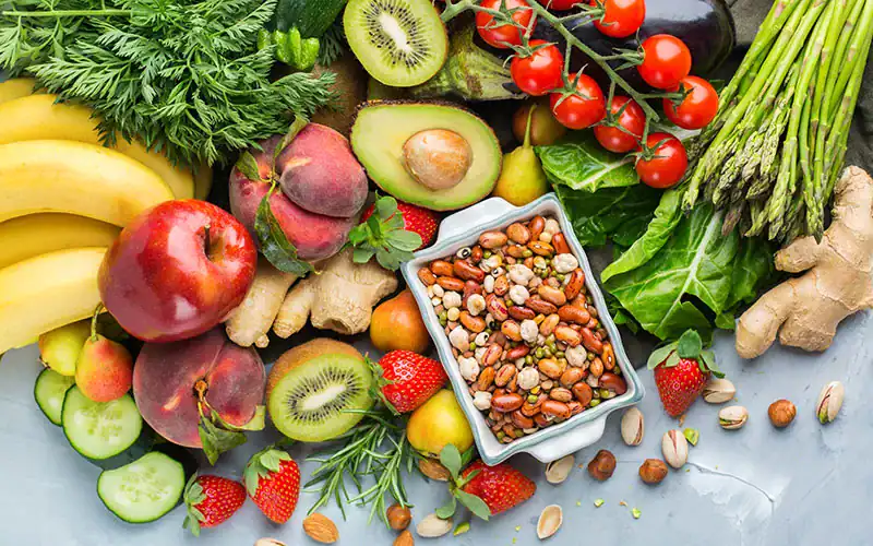 Fresh organic fruits and vegetables including bananas, apples, strawberries, kiwis, avocados, cherry tomatoes, asparagus, ginger, and a variety of beans and nuts, emphasizing healthy eating and produce quality.