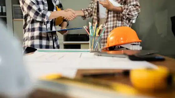 Construction collaboration and handshake between professionals at an architectural or engineering project site.