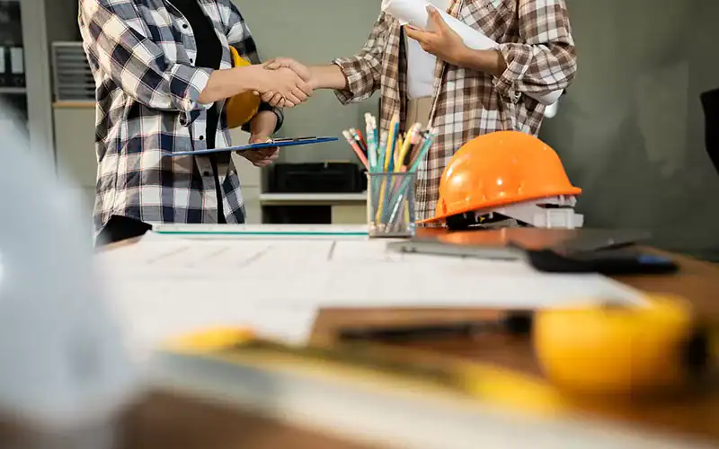 Construction collaboration and handshake between professionals at an architectural or engineering project site.