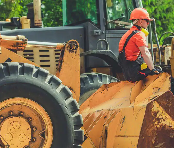 Heavy construction machinery operator sitting on a bulldozer at a construction site with green trees in the background.