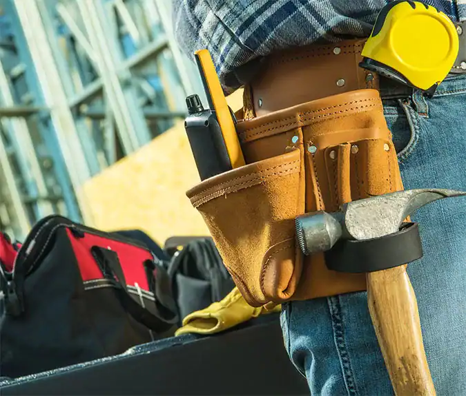 Tool belt with hammer, screwdriver, and safety gear at a construction site, emphasizing skilled trades, construction services, and professional handyman work.