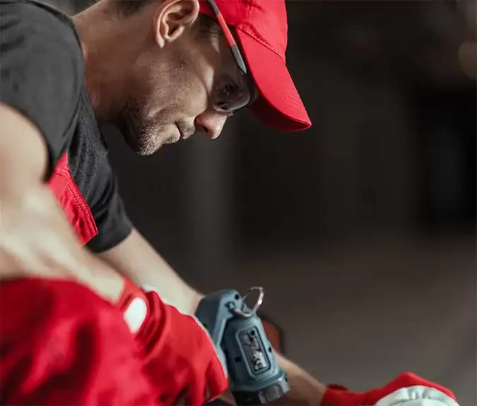High-angle shot of a construction worker using a cordless drill while wearing red work gloves and a red cap, emphasizing professional tools in the construction or industrial environment.