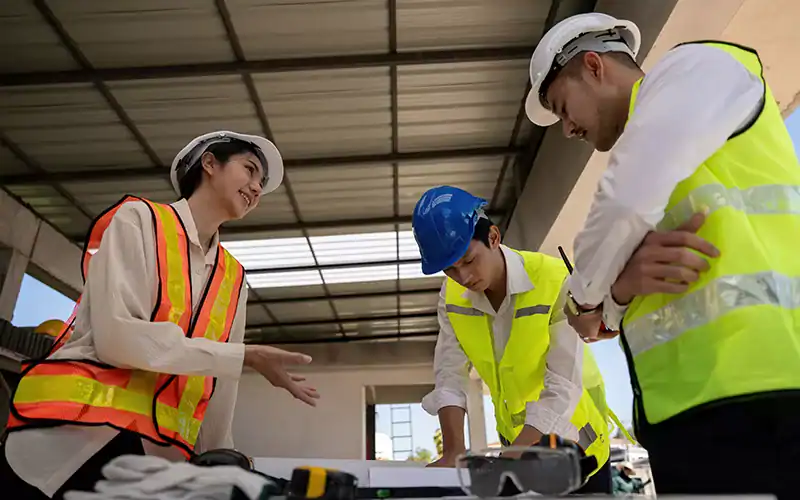 Blue hard hat, construction safety vests, engineers discussing construction plans at RMO Agency construction site, teamwork in building development, project management in construction industry, project planning.
